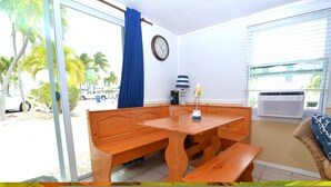 A room with a wooden bench table, a clock on the wall, and a window with blinds.