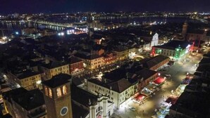 A nighttime view of a historic city center with illuminated buildings, a prominent clock tower, and a waterfront.