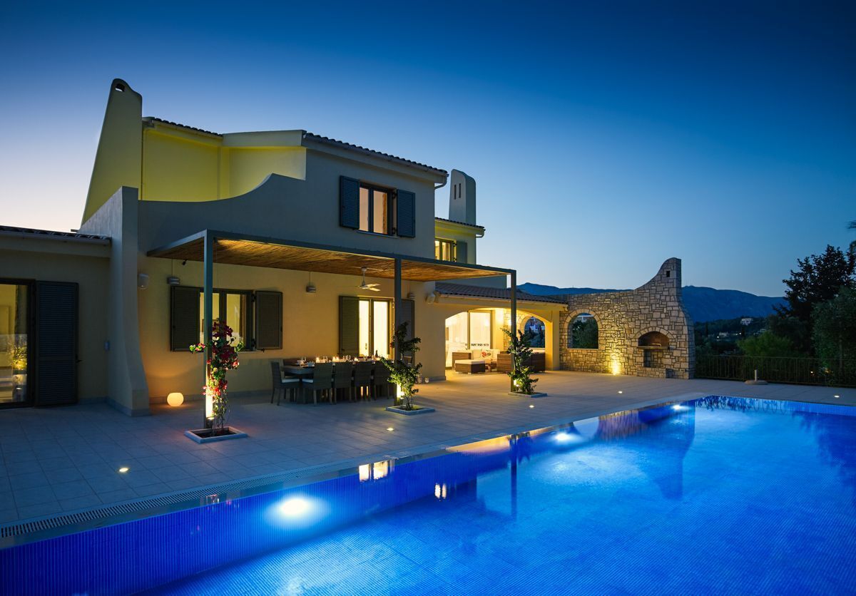 A modern two-story house with a swimming pool, outdoor seating, and stone architecture.