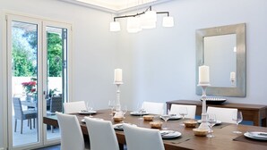 Comedor con una gran mesa de madera dispuesta para seis comensales, sillas blancas, un candelabro y un espejo en la pared.
