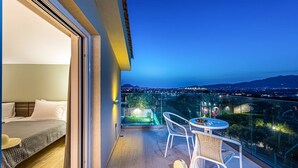 Een balkon met een bed, een tafel en stoelen, met uitzicht op een uitgestrekte stad in de nacht.