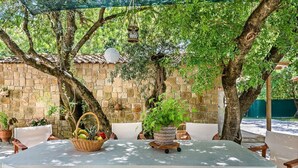 Une terrasse extérieure avec une table et des chaises, entourée d’arbres et d’un mur de pierre.