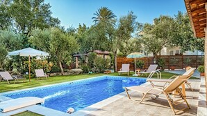 Une piscine entourée d’arbres et d’une clôture en bois, avec des chaises longues et des parasols à proximité.