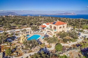 A Mediterranean-style villa with a swimming pool, surrounded by olive trees and a view of the sea.