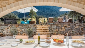 An outdoor dining area with stone walls, a table set for a meal, and a view of the mountains. - Villa Peristeri - Six Bedroom Villa, Sleeps 18 (Apokoronos)
