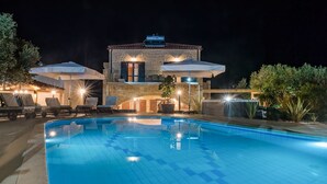 A swimming pool with lounge chairs and umbrellas, a stone building with a chimney, and outdoor lighting. - Villa Peristeri - Six Bedroom Villa, Sleeps 18 (Apokoronos)