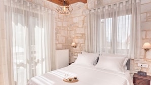 A bedroom with a stone wall, a bed with white linens, a bedside table with a lamp, and a tray with a glass of water and a cup. - Villa Peristeri - Six Bedroom Villa, Sleeps 18 (Apokoronos)