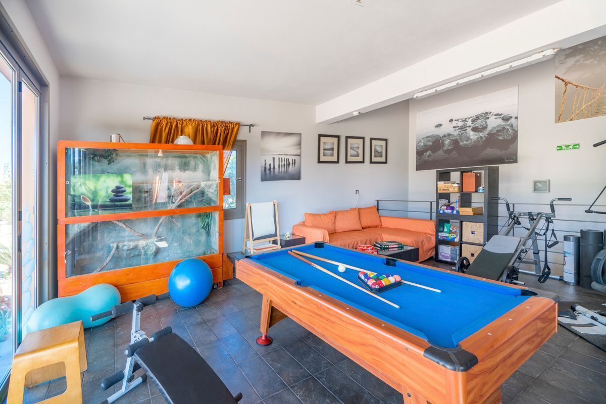 Een moderne kamer met een pooltafel, fitnessapparatuur en een groot raam met uitzicht op het landschap.