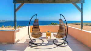 Ein Balkon mit zwei Korbstühlen und einem kleinen Tisch, mit Blick auf die Küste.