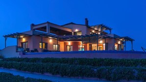 Ein modernes, zweistöckiges Haus mit mehreren Balkonen, großen Fenstern und einer gut beleuchteten Fassade im Abenddämmerung.