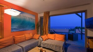 Ein modernes Wohnzimmer mit weitreichendem Meerblick, einer Couch mit orangenen Kissen und einem Tisch mit einer Auflage.
