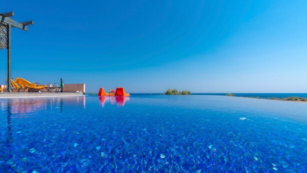 Ein Pool ohne Ende mit klarem, blauem Wasser, eine Holzpergola und orangefarbene Liegestühle.