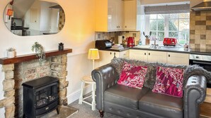 A cozy living room with a fireplace, a leather sofa, and a kitchen in the background.