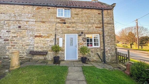A stone house with a tiled roof, a front door, and two windows.