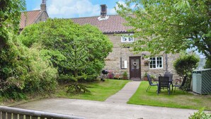 A stone house with a tiled roof, a wooden bench, and a paved pathway leading to a door with a heart-shaped decoration.