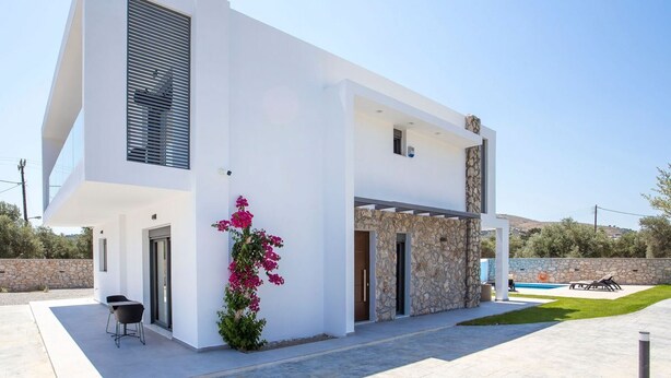Una casa moderna de dos pisos con fachada de piedra, piscina y un patio amueblado al aire libre.
