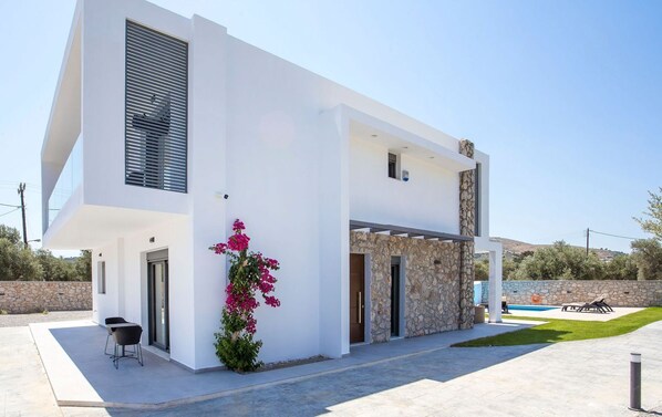Una casa moderna de dos pisos con fachada de piedra, piscina y un patio amueblado al aire libre.