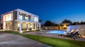 Una casa moderna de dos pisos con fachada de piedra, piscina y mobiliario de exterior.