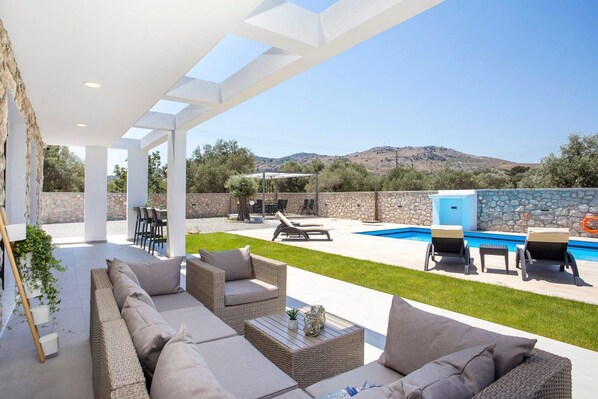 A covered outdoor area with a pool, wicker furniture, and a stone wall.