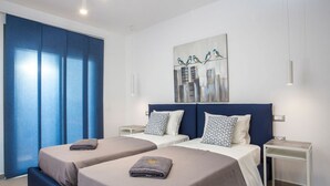 Habitación de hotel con dos camas, un cuadro de un paisaje urbano y una cortina azul.