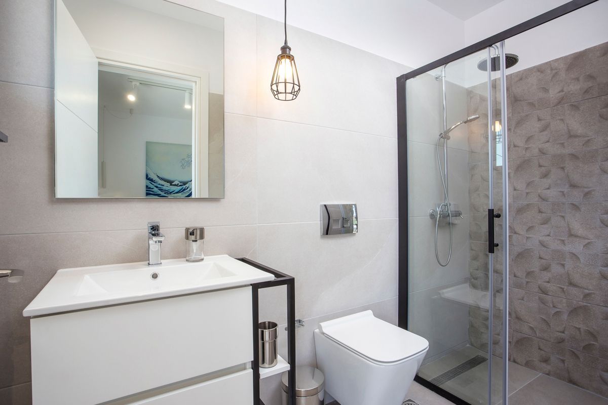 A modern bathroom with a glass-enclosed shower, a white sink, and a large mirror.
