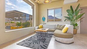 Ein modernes Wohnzimmer mit einer Couch, einem Couchtisch und einem großen Fenster mit Blick auf ein Gebäude und Berge.