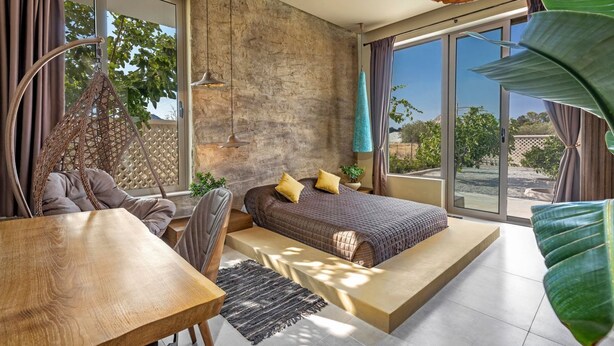 Ein modernes Schlafzimmer mit einem großen Bett, einem Holztisch und Blick ins Freie.