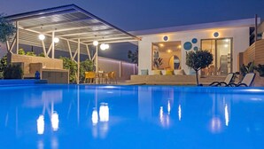 Ein moderner Poolbereich im Freien mit überdachter Lounge, Grillmöglichkeit und gut beleuchtetem Eingang.