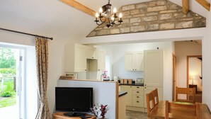 A living room with a TV, wooden furniture, a vase with flowers, and a stone wall. - 2 bedroom accommodation in South Barrow, near Yeovil (South Barrow, near Yeovil)