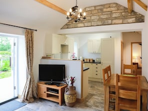 A living room with a TV, wooden furniture, a vase with flowers, and a stone wall.