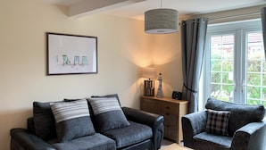 Een woonkamer met een zithoek, een salontafel, een lamp, een lijst met een afbeelding en een raam met gordijnen.