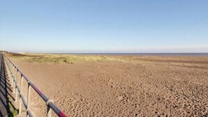 Een kustlandschap met een zandstrand en een metalen hek.