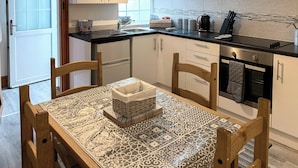 Een moderne keuken met witte kasten, een zwart aanrecht en een eettafel met een tafelkleed met dessin.