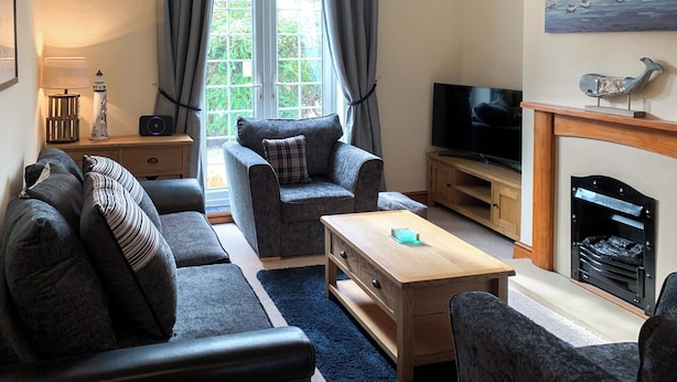 Een woonkamer met een bank, fauteuil, salontafel, televisie, open haard en een schilderij aan de muur.