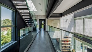 En modern interiör med ett glasräcke, en trappa och utsikt över grönområden utanför.