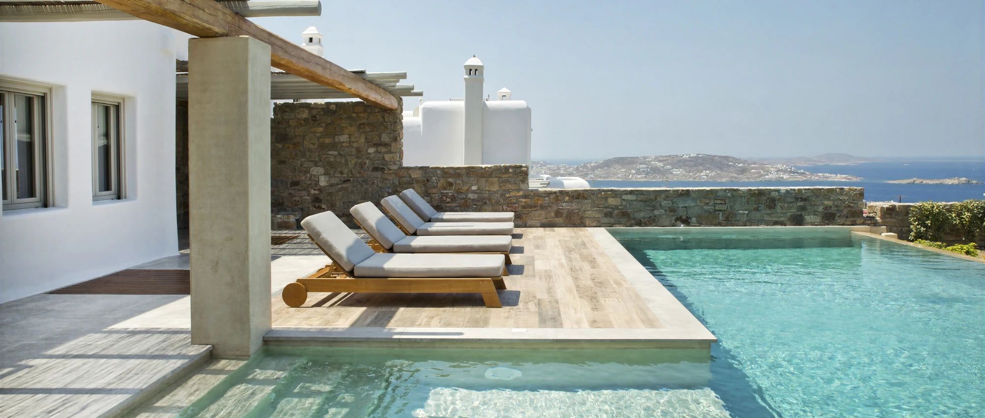 A pool area with lounge chairs and a view of the sea.