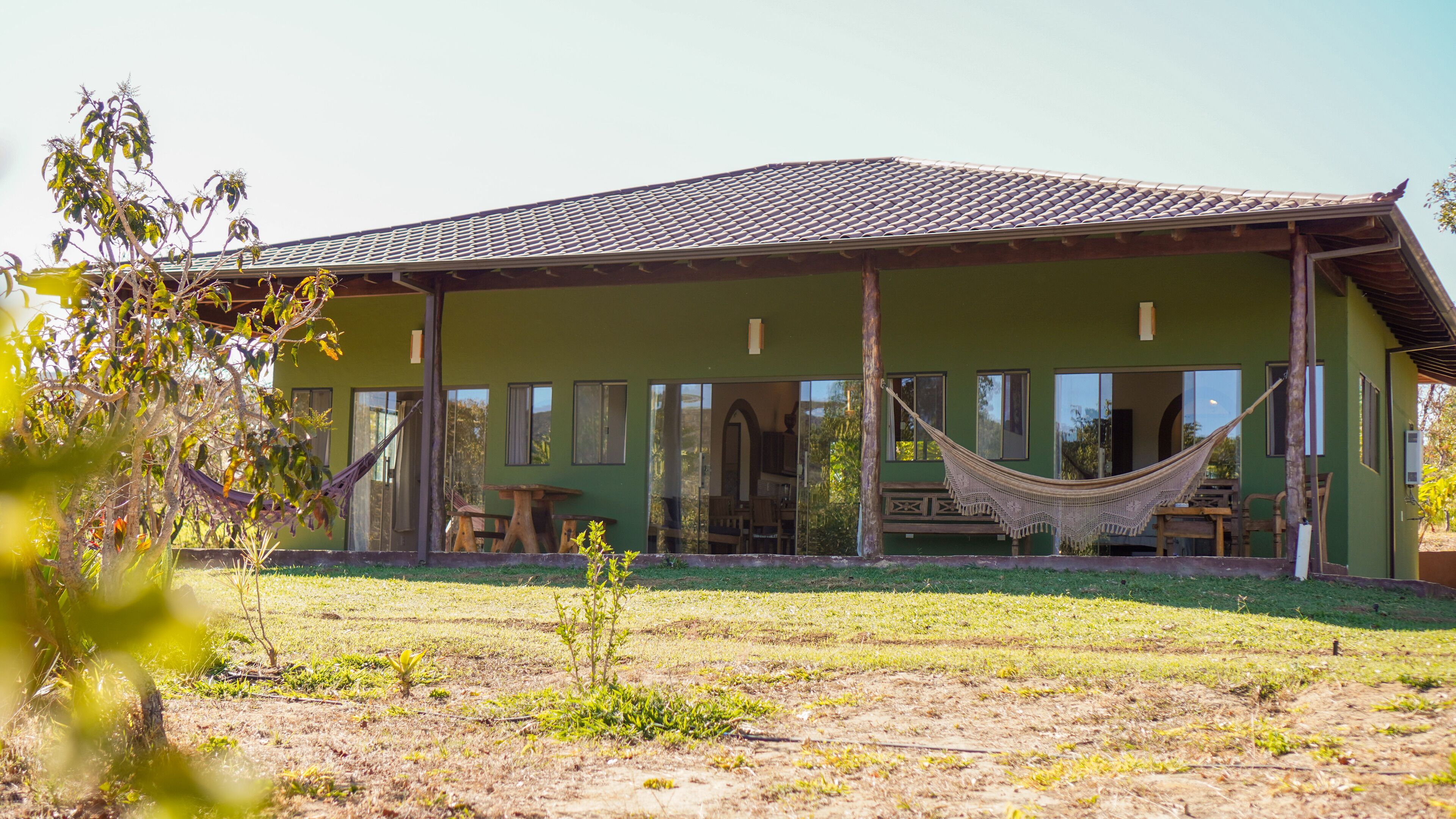 A green building with a tiled roof, large windows, and a hammock in the front.