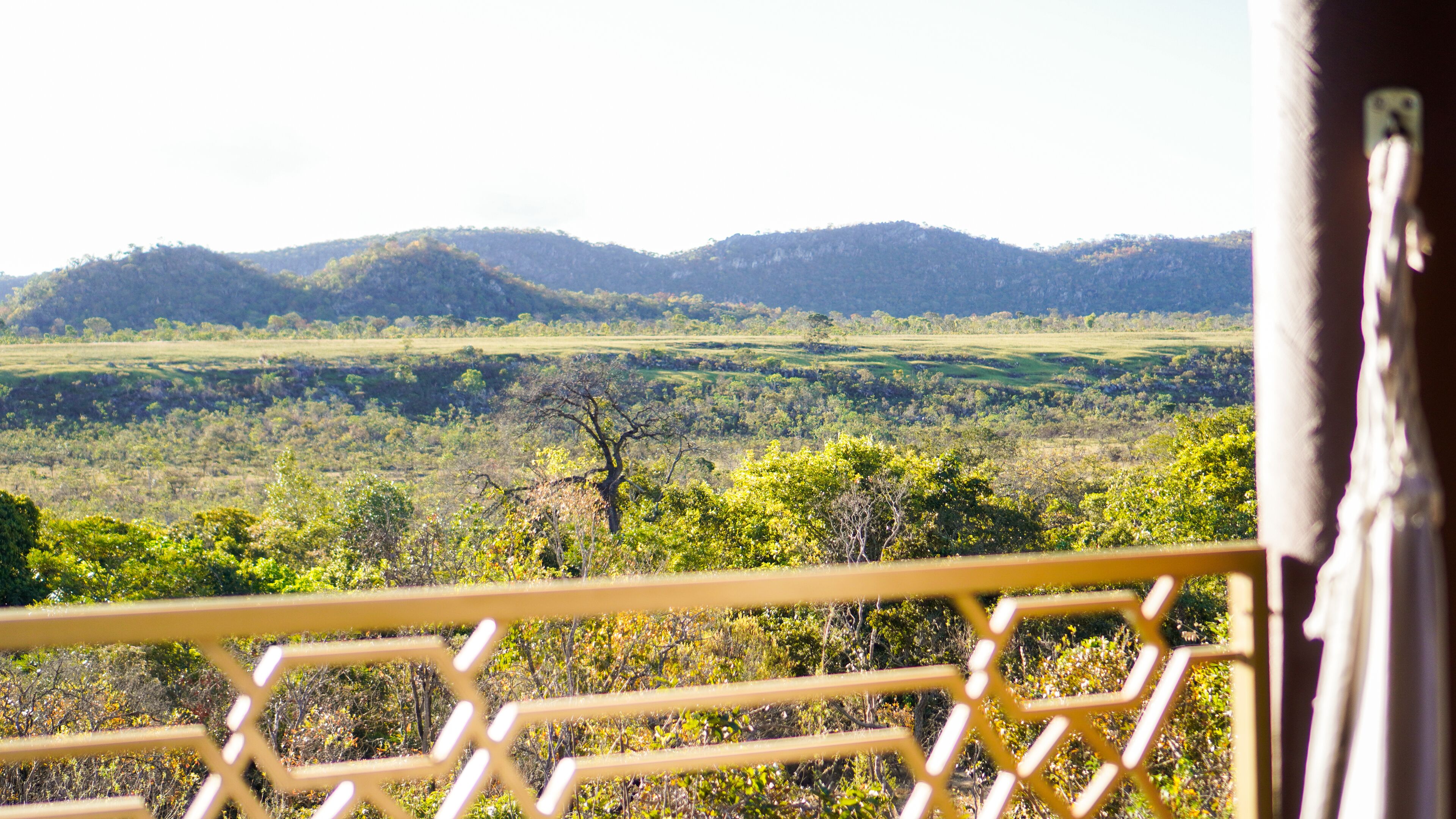 A view from a balcony with a railing, overlooking a landscape with hills and trees.