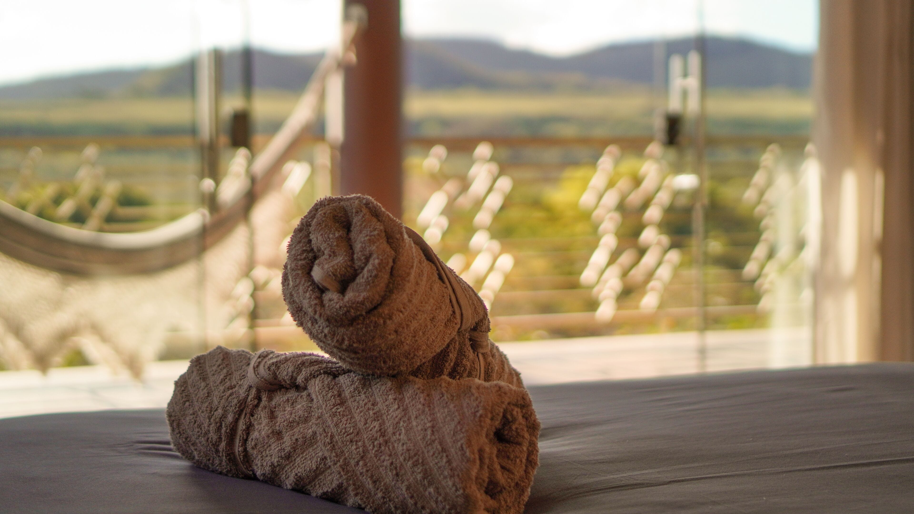 A rolled towel on a bed with a view of a landscape through a window.