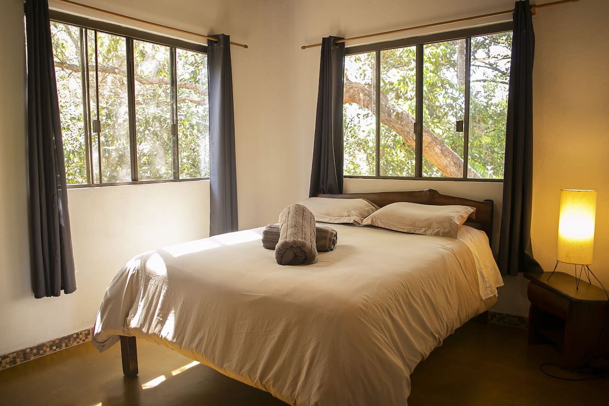 Ein Schlafzimmer mit Bett, Vorhängen, Nachttisch und Lampe.