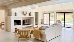 Un salon moderne avec un canapé blanc, un téléviseur et une cheminée. On y trouve également un coin repas avec une table et des chaises.
