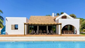 Une maison moderne avec une piscine, un patio couvert doté de sièges et un ciel d’un bleu éclatant.