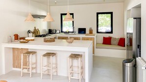 Une cuisine moderne dotée d’un îlot central, de tabourets en bois, de luminaires suspendus en osier et offrant une vue sur l’extérieur grâce à une fenêtre.