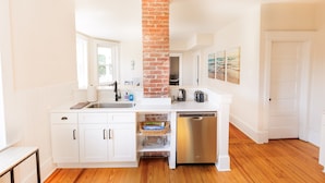 Une cuisine moderne avec des meubles blancs, une colonne en briques, des appareils électroménagers en acier inoxydable et un plancher en bois.