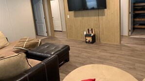 A living room with a large flat-screen TV mounted on the wall, a black leather sofa, and a small table with a card game.