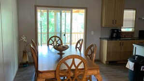 A dining area with a wooden table and chairs, a vase with flowers, and a view of the outdoors through a glass door.