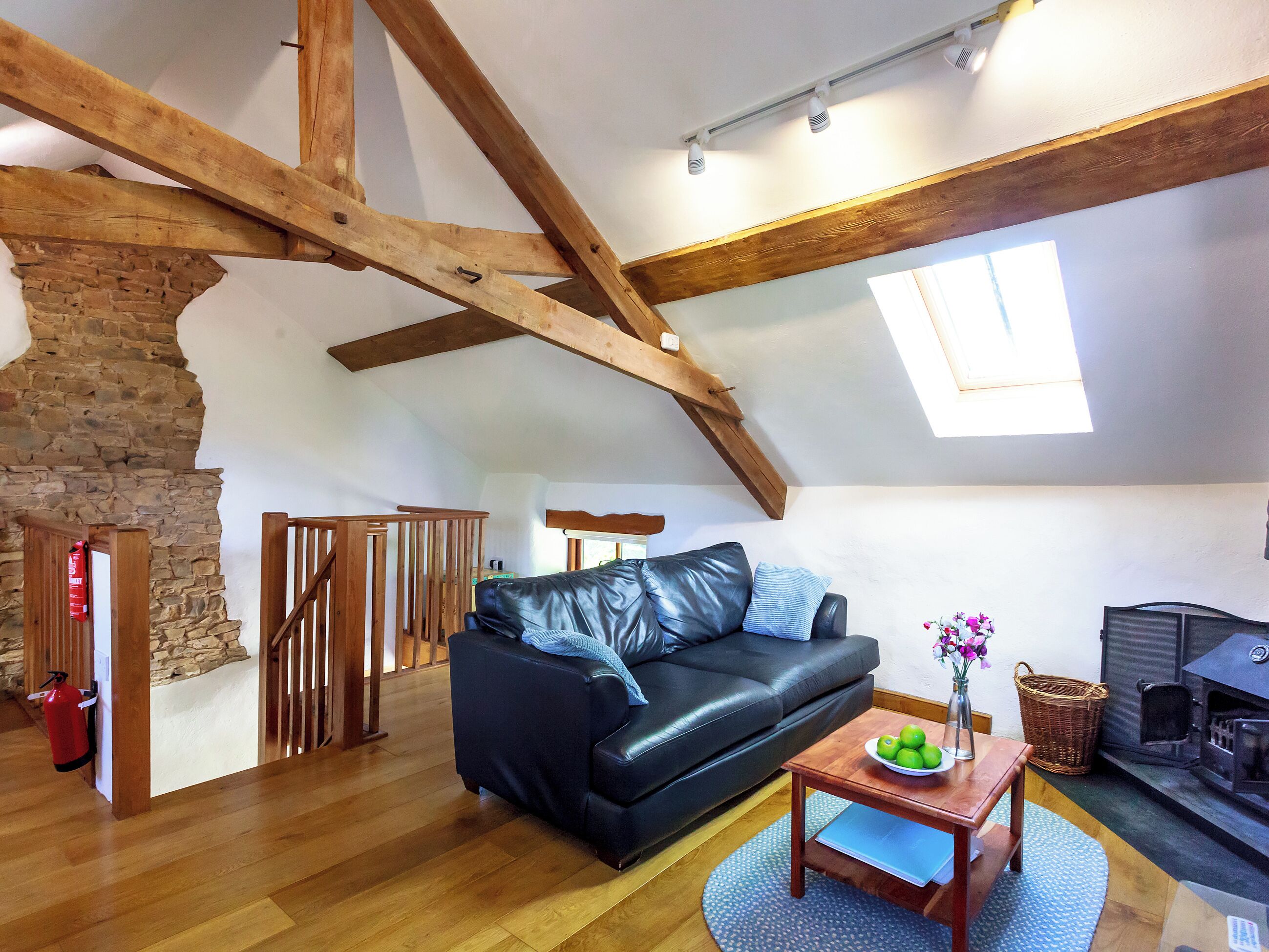 Ein gemütliches Wohnzimmer mit einer schwarzen Ledersofa, Holzbalken, einer Steinwand, einem Kamin und einem Holztisch mit Äpfeln.