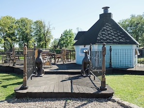 Une terrasse en bois avec une clôture en métal, un petit bâtiment doté d’un toit noir et une statue de chien.