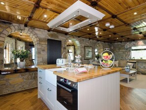 A kitchen with stone walls, wooden ceiling, and a central island with a Bosch oven.