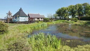 Un paysage rural avec une maison, un étang et un pont.